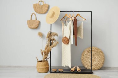 Beyaz duvarın yanında şık kıyafetler ve hasır aksesuarlarla siyah askılar.