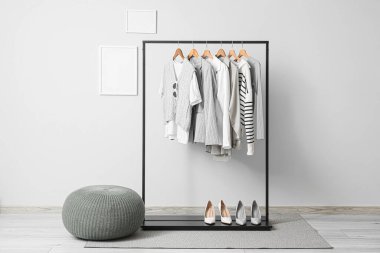 Beyaz duvarın yanındaki siyah askıda şık kıyafetler ve ayakkabılar var.