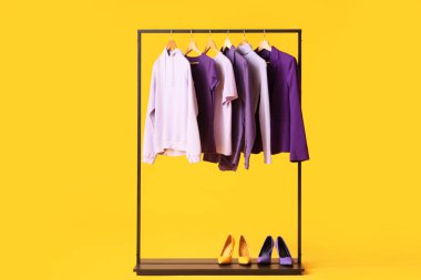 Siyah askılar şık kıyafetler ve sarı arka planda ayakkabılar.