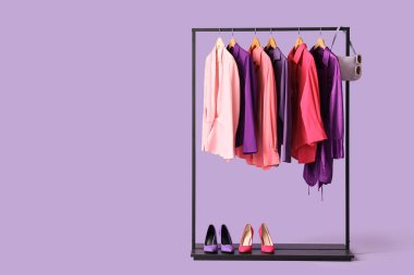 Mor arka planda şık kıyafetler, ayakkabılar ve aksesuarlar olan siyah askılar.