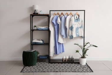 Odasında beyaz duvarın yanında giysileri olan raf ve dizme ünitesi.