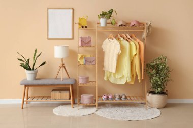 Odada bej duvarın yanında şık kıyafetler, aksesuarlar ve ayakkabılar var.