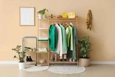 Bej duvarın yanında şık kıyafetler, ayakkabılar ve aksesuarlarla dolu bir oda.