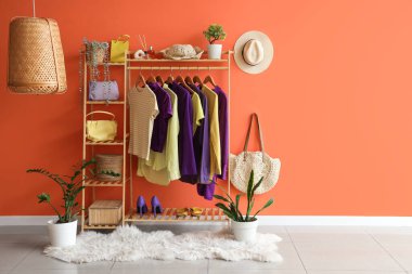 Şık kıyafetler, aksesuarlar ve turuncu duvarın yanında ayakkabılar.