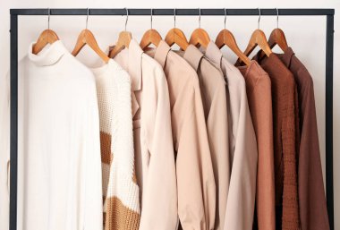 Beyaz duvarın yanında asılı giysilerle dizilin, kapatın.