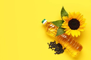 Ayçiçekli bir şişe yağ ve sarı arka planda tohumlar.