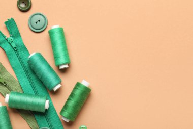 Yeşil iplik makaralı kompozisyon, fermuarlar ve bej arkaplandaki düğmeler, yakın plan