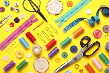 Sarı arka planda farklı iplik makaraları ve dikiş aksesuarlarıyla kompozisyon