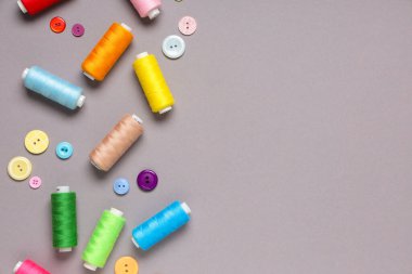 Gri arkaplanda farklı iplik makaraları ve düğmeler