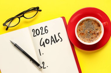 Listesi boş bir defter, sarı arka planda gözlük ve bir fincan kahve. Yeni yıl hedefleri