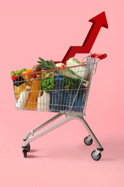Pembe arka planda yiyecek dolu alışveriş arabası.