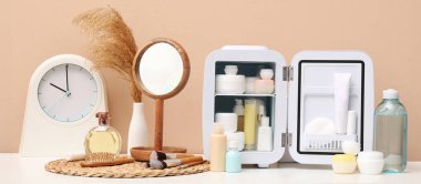 Kozmetik ürünleri, ayna ve saati olan küçük buzdolabı kahverengi duvara karşı.