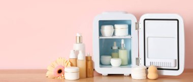 Kozmetik ürünleri ve pembe arka planda çiçek olan küçük bir buzdolabı. Yakın çekim.