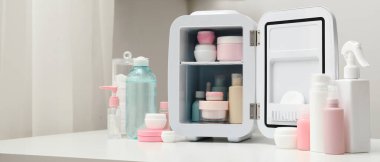 Beyaz duvarda kozmetik ürünleri olan küçük bir buzdolabı.