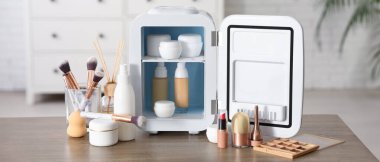 Beyaz duvarın yanındaki masada kremalı ve temeli olan küçük bir kozmetik buzdolabı. Yakın çekim.