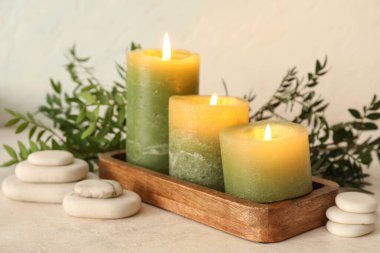 Mumlar, ahşap tepsi, spa taşları ve yeşil yapraklı spa kompozisyonu.