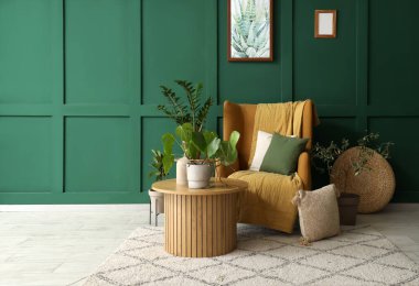 Yeşil duvarın yanında rahat koltuğu, masası ve çiçekleri olan şık bir oturma odası.