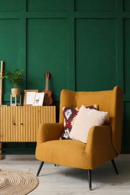 Yeşil duvarın yanında rahat koltuğu ve çekmeceleri olan şık bir oturma odası.