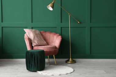 Oturma odasındaki yeşil duvarın yanında rahat koltuk, puf ve zemin lambası.