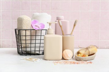 Şişeler dolusu kozmetik ürünler ve sepet pembe fayans duvarının yanındaki ışık masasında farklı banyo malzemeleri.