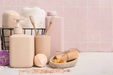 Şişeler dolusu kozmetik ürünler ve sepet pembe fayans duvarının yanındaki ışık masasında farklı banyo malzemeleri.