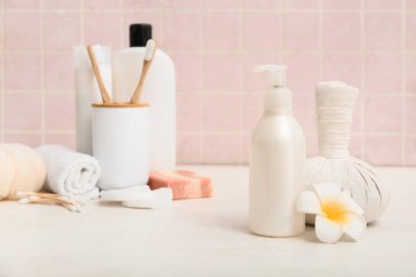 Bir şişe kozmetik ürünü, bitkisel masaj çantası ve arka planda çiçek, yakın plan.