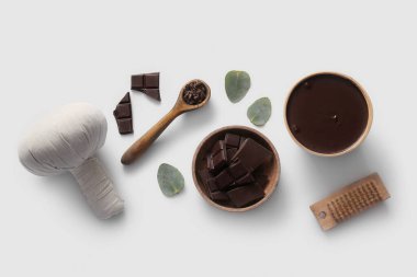 Bitkisel masaj torbası, kase parçaları ve beyaz arka planda erimiş çikolatalı spa kompozisyonu.