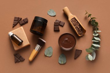Kahverengi arka planda bir kase erimiş çikolata, ahşap kepçe ve makyaj fırçası ile spa kompozisyonu