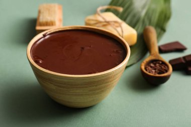 Yeşil arka planda spa işlemi için bir kase erimiş çikolatalı spa kompozisyonu, yakın plan.