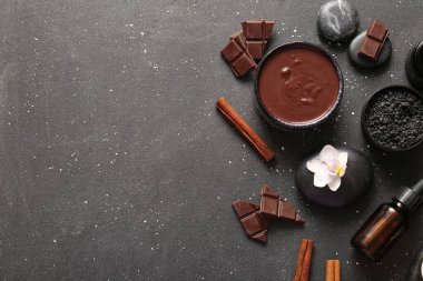Bir kase erimiş çikolatalı spa kompozisyonu, çikolata parçaları ve siyah arka planda spa taşları
