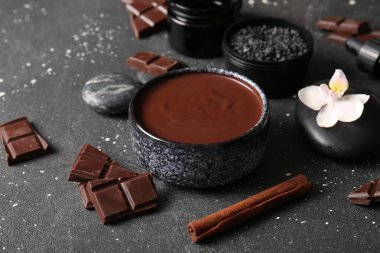 Bir kase erimiş çikolatalı spa kompozisyonu, çikolata parçaları ve tarçın çubuğu siyah arka planda, yakın plan