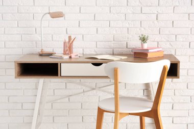 Masa lambası, masa üzerinde farklı okul kırtasiyesi ve beyaz tuğla duvarın yanında sandalye.