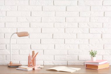 Masa lambası ve okul kırtasiyesi beyaz tuğla duvarın yanındaki masada.