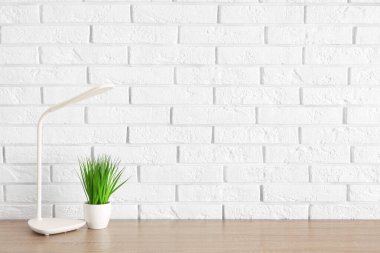 Masa lambası ve çiçek beyaz tuğla duvarın yanında.