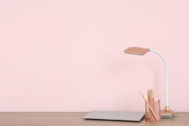 Modern dizüstü bilgisayar ve masa lambası odada, pembe duvarın yanında.
