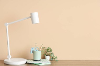 Oda içinde bej duvar yakınında masa lambası, ev bitkisi ve ofis malzemesi olan modern işyeri