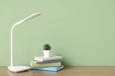 Modern masa lambası, çiçek ve kitaplar yeşil duvarın yanındaki odada.