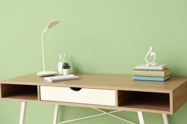 Masa lambasının, ev bitkisinin ve ofis malzemelerinin bulunduğu modern işyeri yeşil duvarın yanındaki odada.