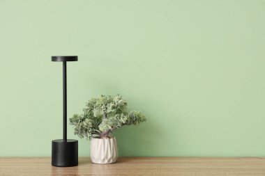 Modern masa lambası ve çiçek yeşil duvarın yanındaki masada.