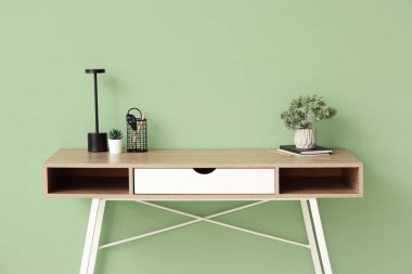 Modern masa lambası, ev bitkileri ve ofis malzemeleri yeşil duvarın yanındaki masada.