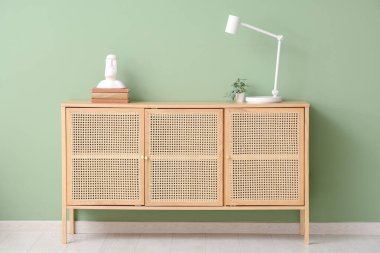 Modern masa lambası, ev bitkisi, heykel ve çekmecelerdeki çekmeceler, oda yeşil duvarın yanında.