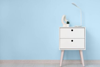 Masa lambası, çiçek ve biblo mavi duvarın yanındaki odada.