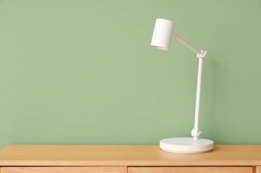 Odadaki yeşil duvarın yanındaki çekmecelerin üzerindeki masa lambası.