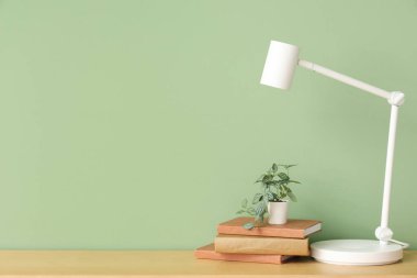 Modern masa lambası, çiçek ve kitaplar yeşil duvarın yanındaki odada.