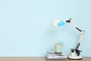 Masa lambası, ofis malzemeleri ve mavi duvarın yanındaki ev bitkisi olan modern işyeri.
