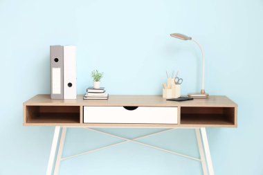 Masa lambası, ofis gereçleri ve mavi duvarın yanındaki ev bitkisi olan güzel bir iş yeri.