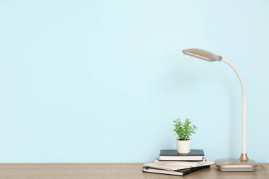 Masa lambası, çiçek ve defterler mavi duvarın yanındaki odada.