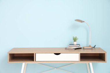 Masa lambası, çiçek ve defterler mavi duvarın yanındaki odada.