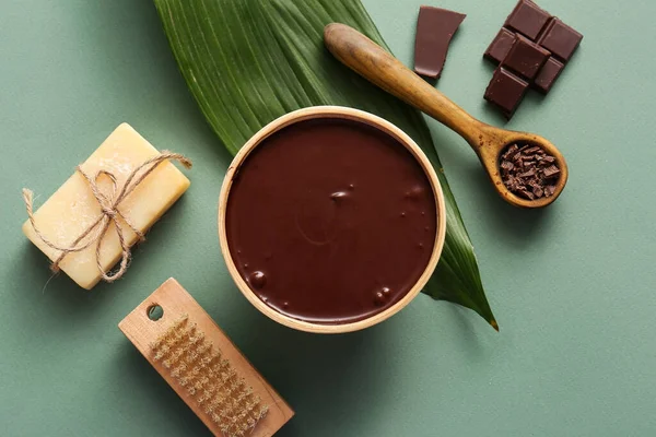 Yeşil arka planda bir kase erimiş çikolata, sabun ve yeşil yaprak içeren spa kompozisyonu