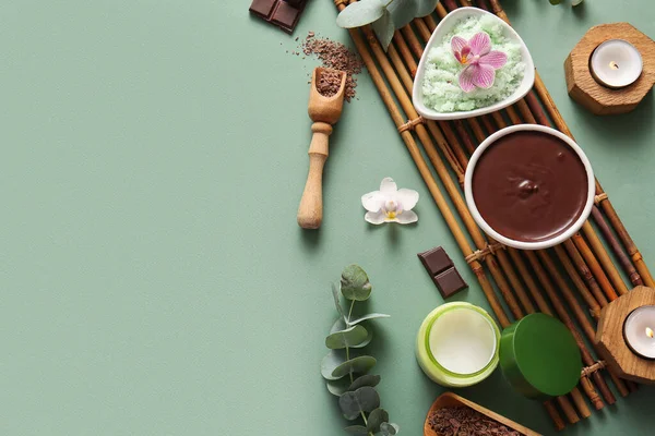Bambu tepsisiyle spa kompozisyonu, bir kase erimiş çikolata, yanan mumlar ve yeşil arka planda çiçekler.